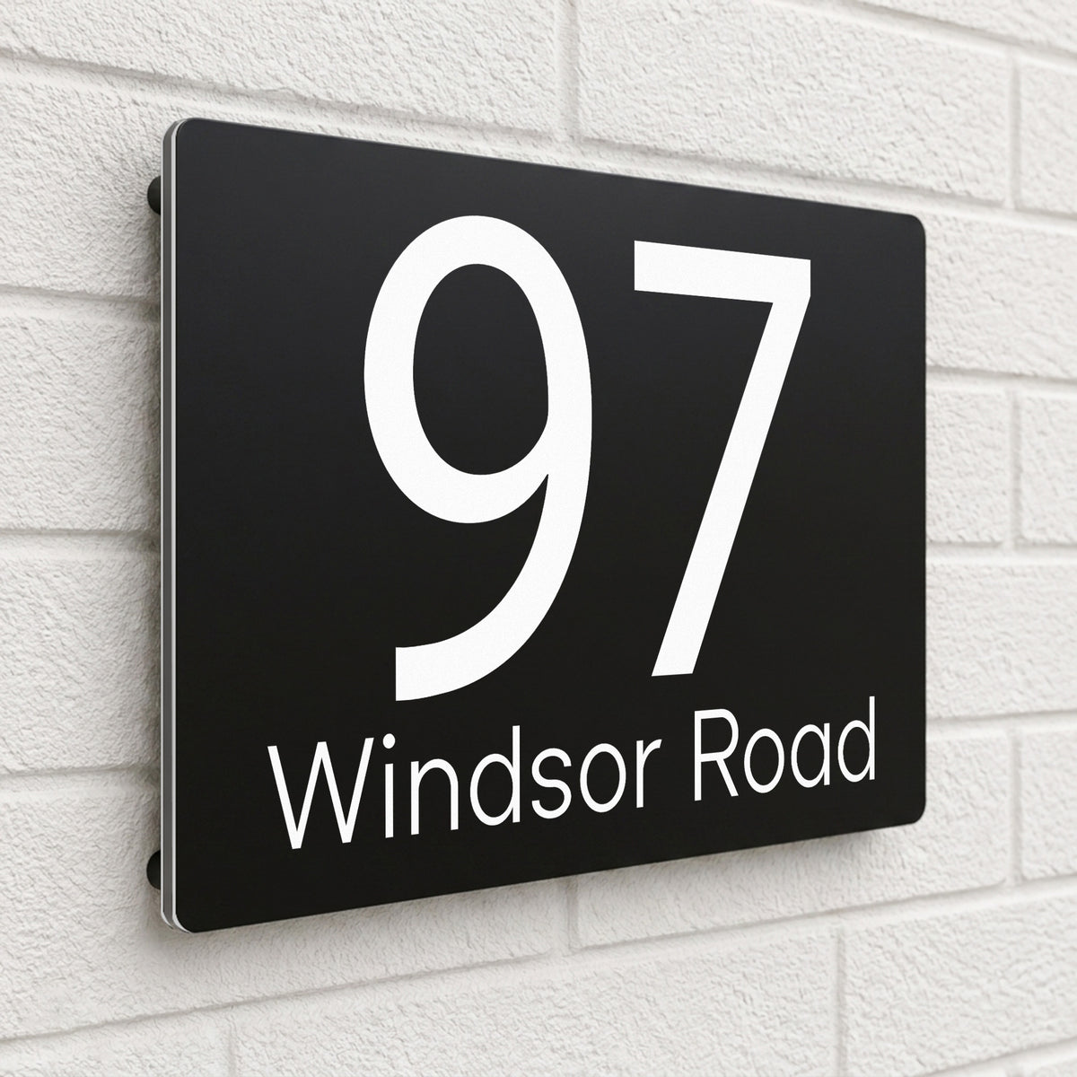 Black personalised house number sign reading '97 Windsor Road' mounted on a white brick wall - SignStation composite aluminium house sign