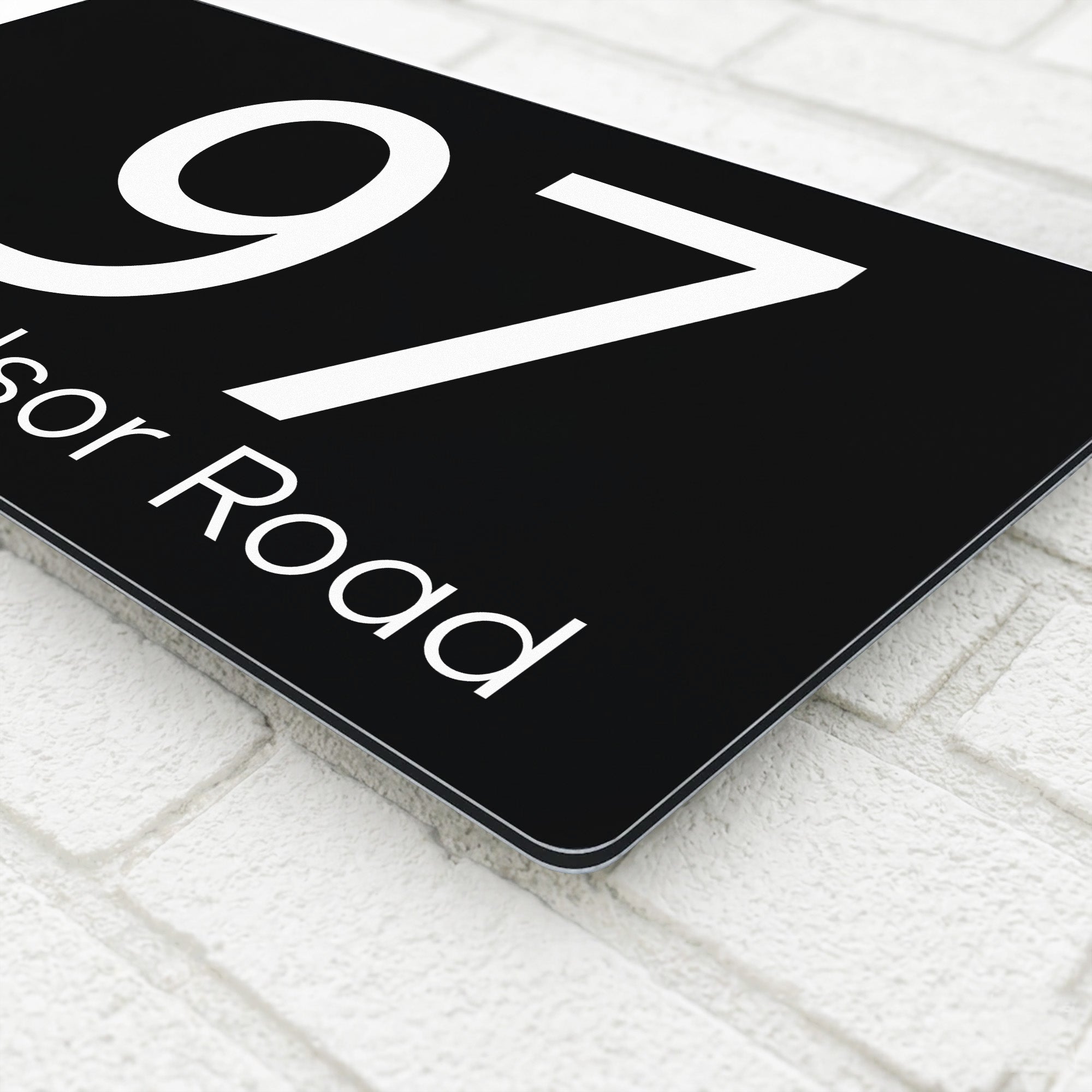 Close-up corner detail of a black composite aluminium house sign showing the polished edge and mounting finish