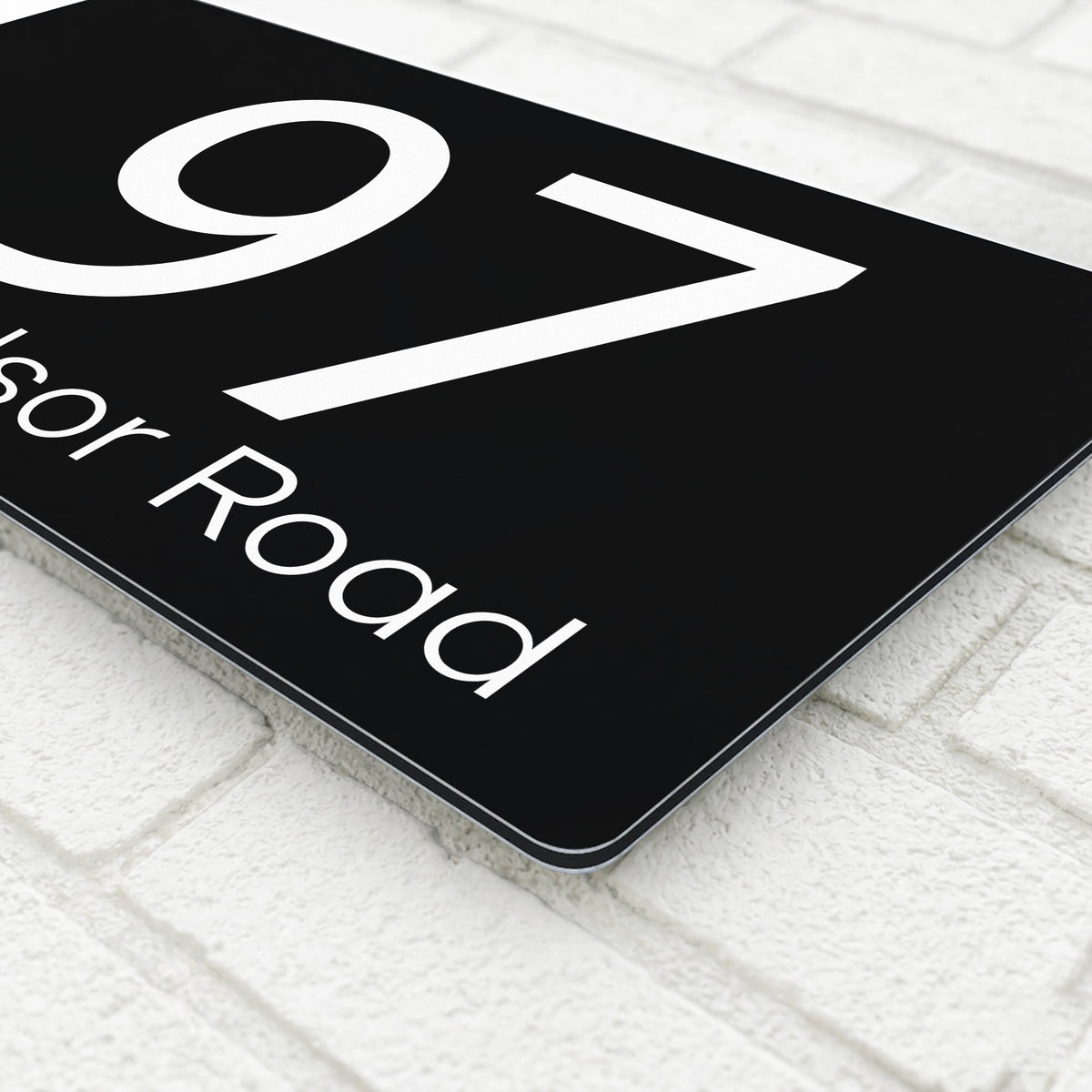 Close-up corner detail of a black composite aluminium house sign showing the polished edge and mounting finish