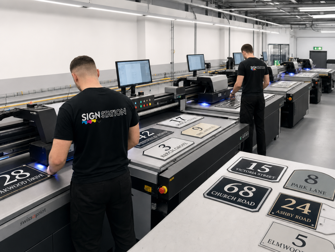 Wide view of the SignStation production floor with staff operating UV flatbed printers and finished house signs on the bench